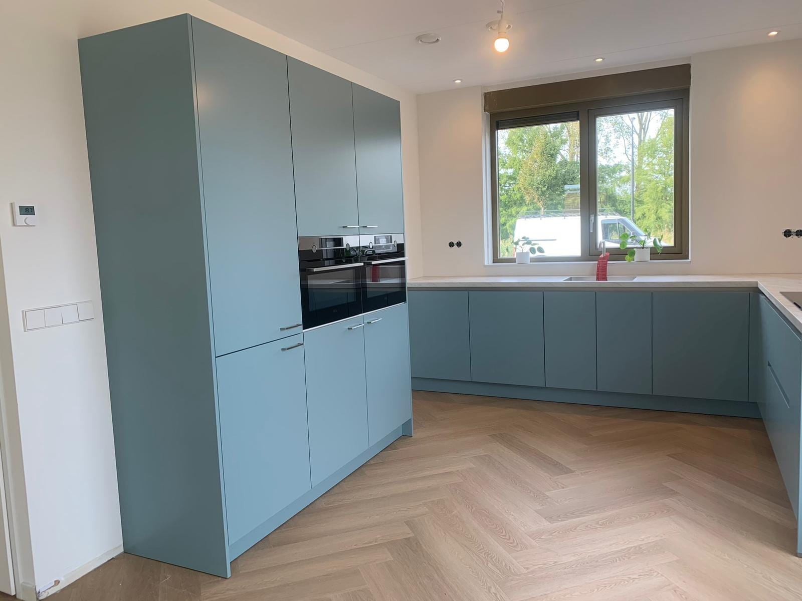 Blauwgrijze keuken in L-opstelling met visgraatvloer