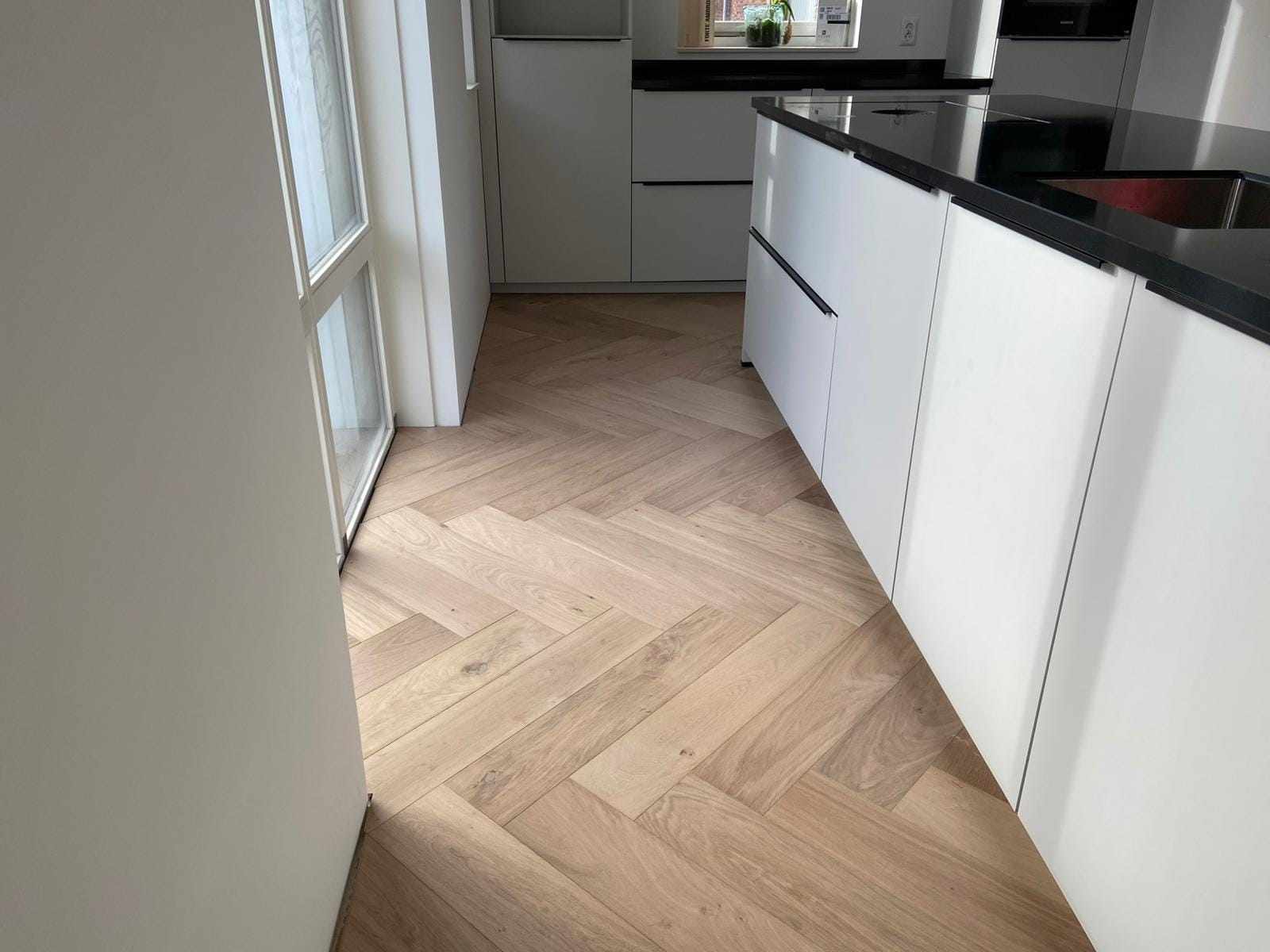 Visgraatvloer langs een witte keuken